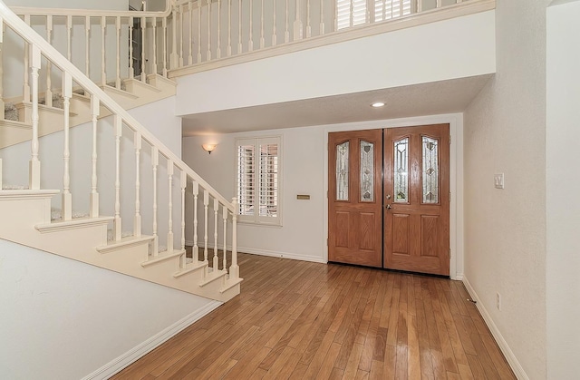 entryway with stairway, wood finished floors, a towering ceiling, and baseboards