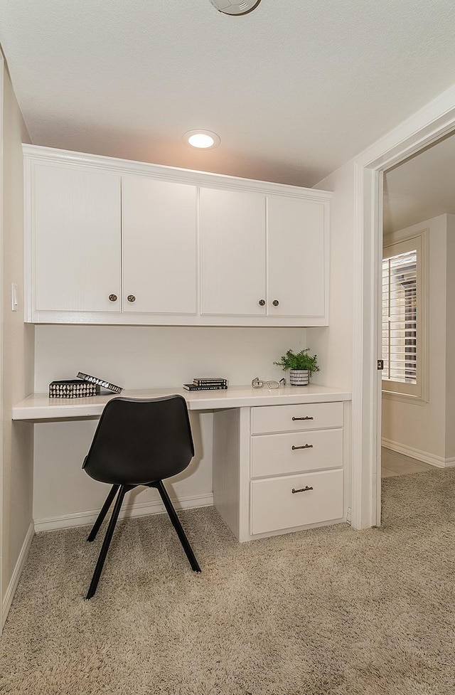 office area with baseboards, built in desk, and light colored carpet