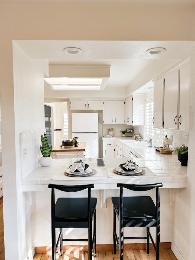 kitchen featuring freestanding refrigerator, white cabinetry, tile countertops, and a peninsula