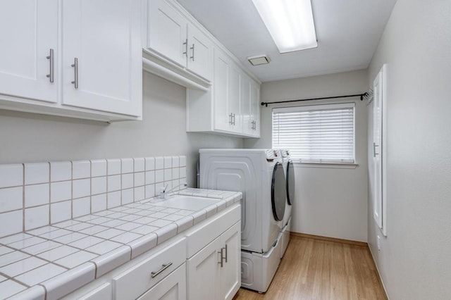 washroom with light wood finished floors, cabinet space, a sink, separate washer and dryer, and baseboards