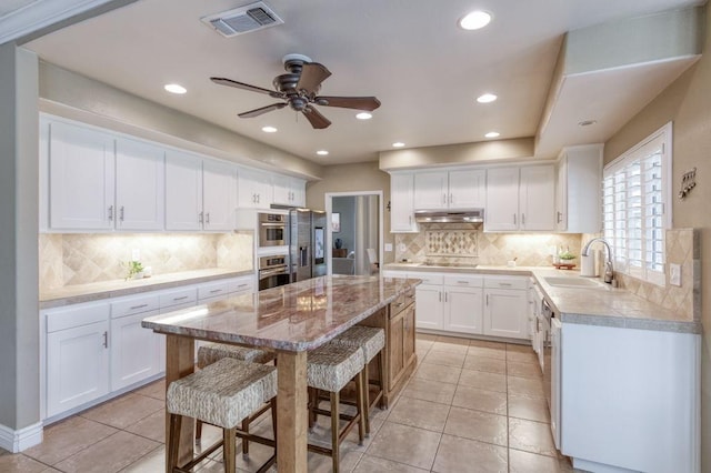 kitchen with appliances with stainless steel finishes, white cabinetry, a kitchen island, a sink, and a kitchen breakfast bar