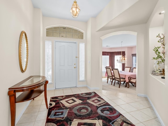 entrance foyer featuring light tile patterned floors, baseboards, arched walkways, and a chandelier