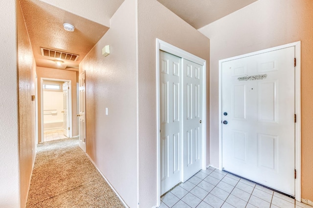 foyer entrance featuring light tile patterned floors, a textured wall, a textured ceiling, and visible vents