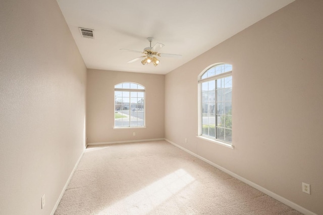 spare room featuring light carpet, ceiling fan, visible vents, and baseboards