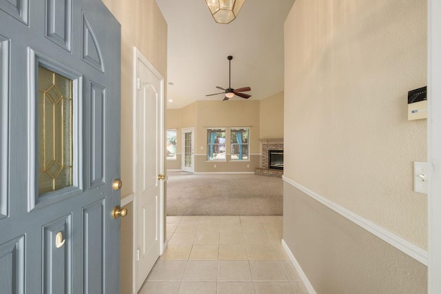 interior space featuring a fireplace, light tile patterned floors, light colored carpet, a ceiling fan, and baseboards