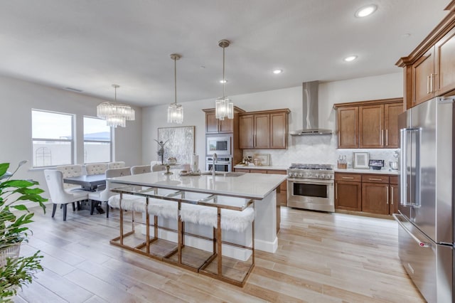 6375 E Millie Dr, Fresno, CA 93727 - kitchen with premium appliances, wall chimney exhaust hood, light countertops, brown cabinetry, and a kitchen breakfast bar