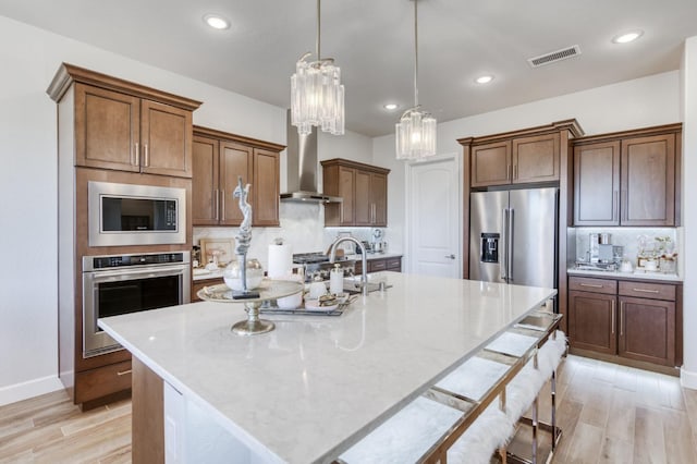 6375 E Millie Dr, Fresno, CA 93727 - kitchen with appliances with stainless steel finishes, wall chimney exhaust hood, a kitchen island with sink, light wood-style flooring, and decorative backsplash