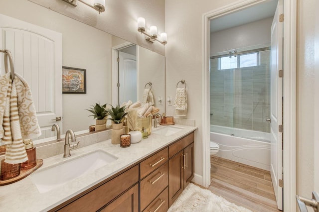 full bath with bath / shower combo with glass door, a sink, toilet, and double vanity