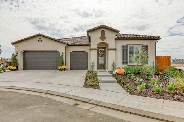 mediterranean / spanish-style home with a tile roof, stucco siding, an attached garage, fence, and driveway