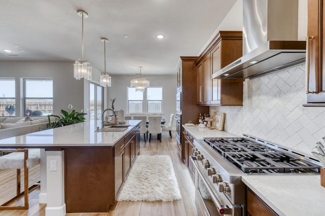 6375 E Millie Dr, Fresno, CA 93727 - kitchen with wall chimney range hood, a sink, light wood-style floors, appliances with stainless steel finishes, and an island with sink