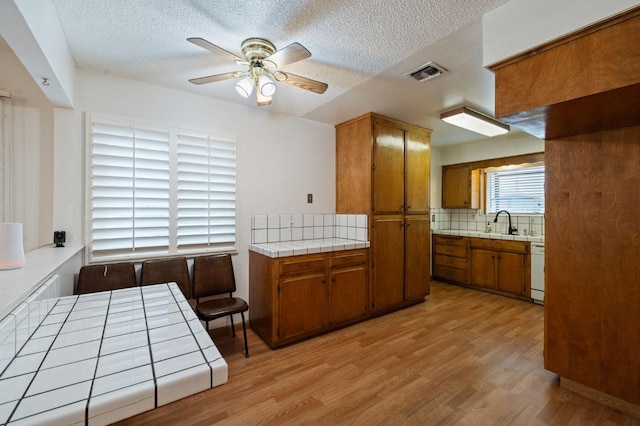 kitchen featuring light wood finished floors, visible vents, tile counters, decorative backsplash, and brown cabinets