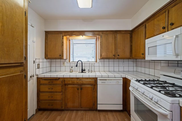 kitchen featuring tile countertops, light wood-style flooring, white appliances, a sink, and brown cabinets