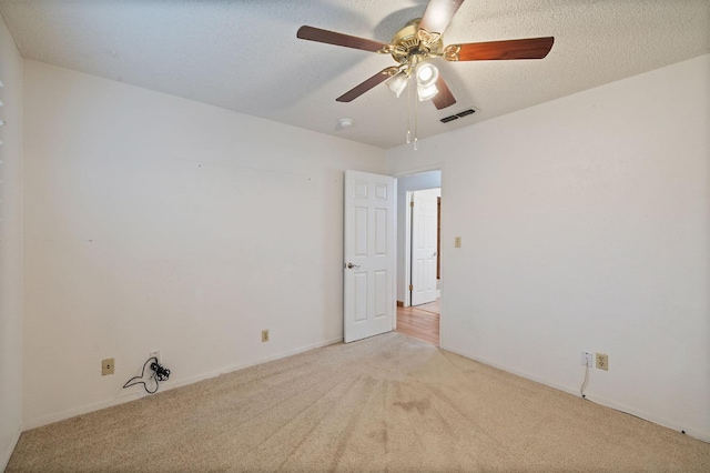 spare room with light carpet, ceiling fan, visible vents, and a textured ceiling