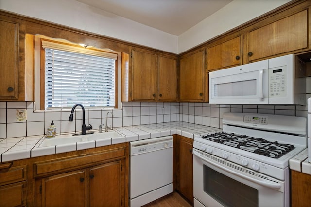 kitchen with tile counters, white appliances, brown cabinets, and a sink