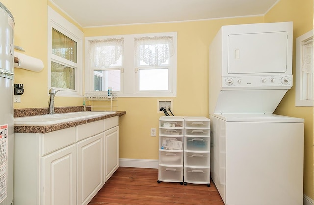 washroom featuring stacked washer and dryer, cabinet space, a sink, wood finished floors, and baseboards