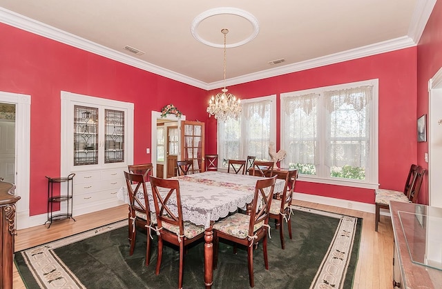 dining space with an inviting chandelier, ornamental molding, wood finished floors, and visible vents