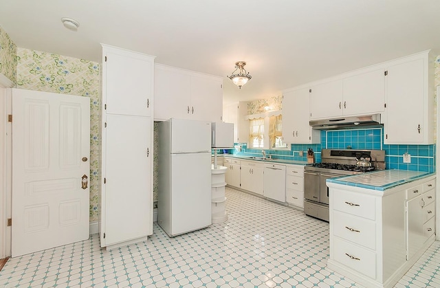 kitchen with tile counters, white cabinets, a sink, white appliances, and under cabinet range hood