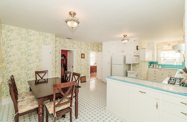 kitchen featuring wallpapered walls, white appliances, white cabinets, tile countertops, and ventilation hood