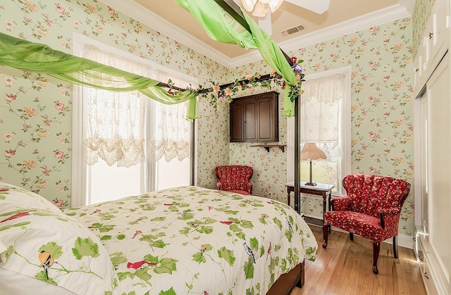 bedroom featuring wallpapered walls, visible vents, ornamental molding, and light wood-style floors