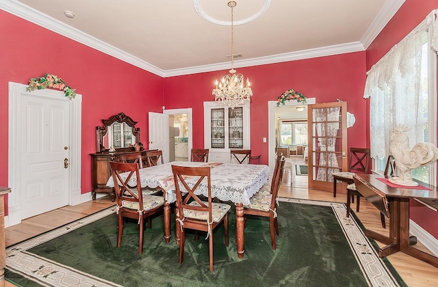 dining room featuring a notable chandelier, wood finished floors, visible vents, baseboards, and ornamental molding