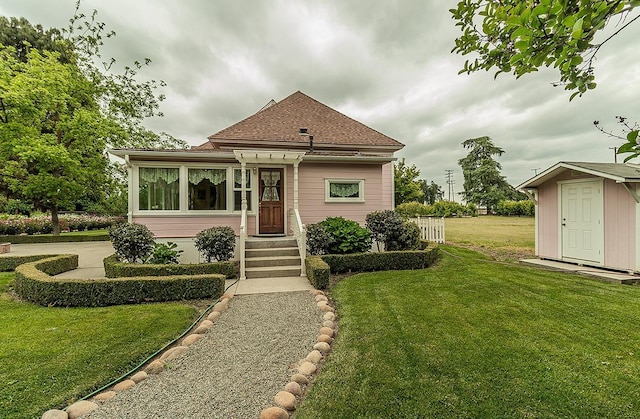 view of front of house with a storage unit, a shingled roof, a front lawn, and an outbuilding