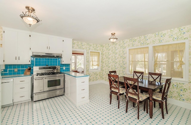kitchen with baseboards, wallpapered walls, under cabinet range hood, white cabinets, and double oven range