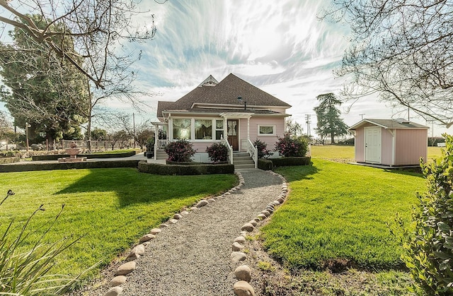 view of front of house with a shingled roof, an outdoor structure, a front yard, and a storage unit