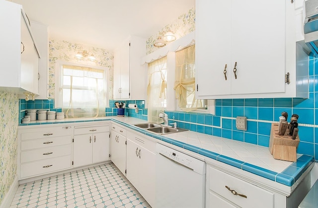 kitchen with dishwasher, wallpapered walls, a sink, and white cabinets