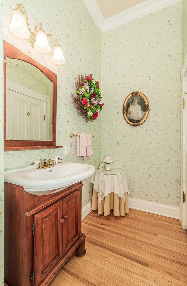 bathroom featuring wood finished floors, vanity, baseboards, ornamental molding, and wallpapered walls