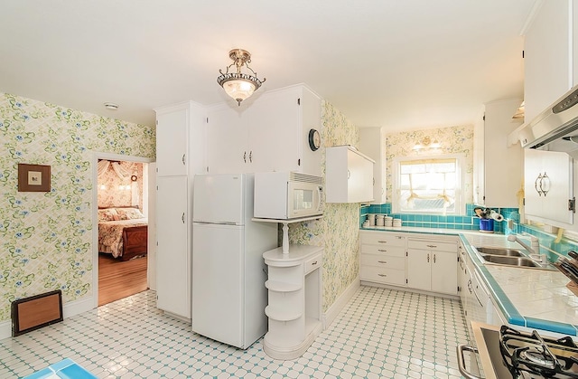 kitchen with tile counters, a sink, white appliances, and wallpapered walls