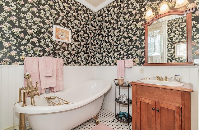 full bathroom with a wainscoted wall, ornamental molding, vanity, a freestanding tub, and wallpapered walls