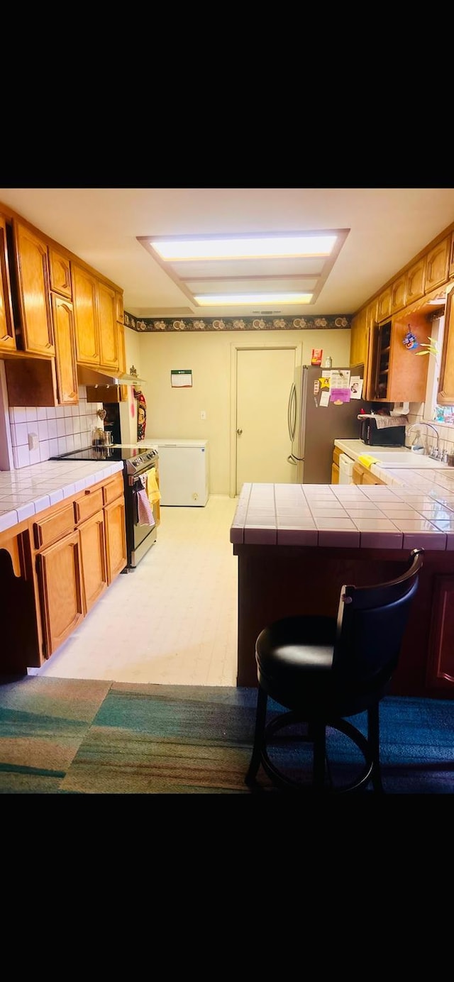 kitchen with tile countertops, tasteful backsplash, a breakfast bar area, and freestanding refrigerator