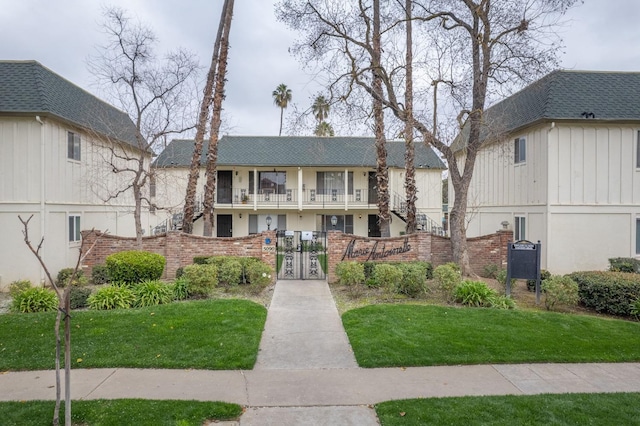 view of front of house with a fenced front yard, brick siding, roof with shingles, a gate, and a balcony