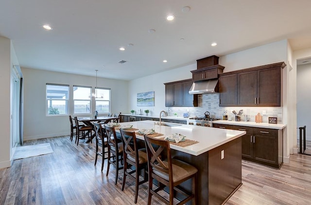 1048 Sawtooth Way S, Madera, CA 93636 - kitchen with a kitchen island with sink, light countertops, dark brown cabinetry, decorative backsplash, and light wood-style flooring