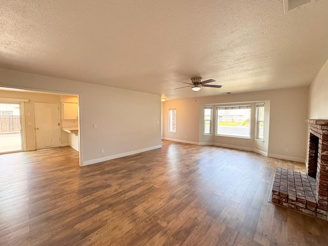 unfurnished living room featuring ceiling fan, wood finished floors, visible vents, baseboards, and a brick fireplace