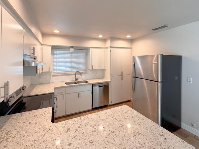 kitchen with appliances with stainless steel finishes, white cabinets, a sink, and under cabinet range hood