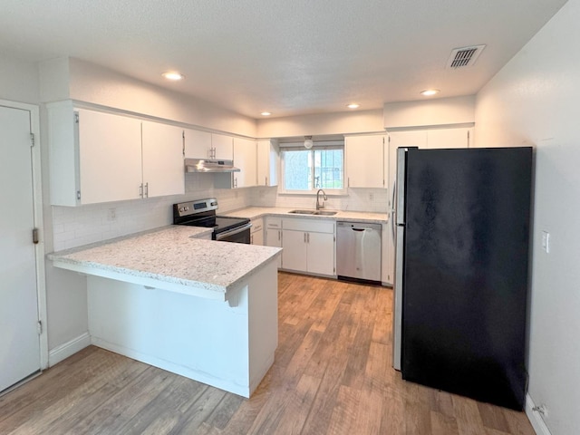 kitchen with appliances with stainless steel finishes, white cabinets, a sink, a peninsula, and under cabinet range hood