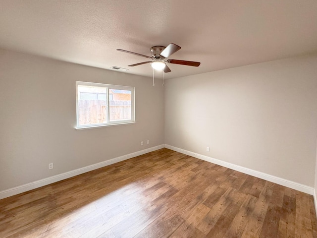 spare room featuring a textured ceiling, wood finished floors, visible vents, and baseboards