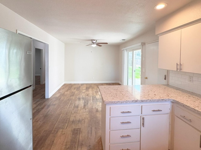 kitchen featuring a peninsula, light stone counters, freestanding refrigerator, and white cabinets