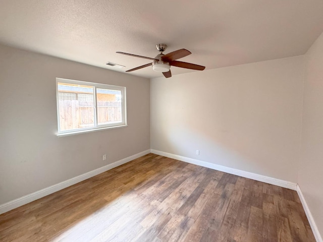 empty room with baseboards, visible vents, ceiling fan, wood finished floors, and a textured ceiling