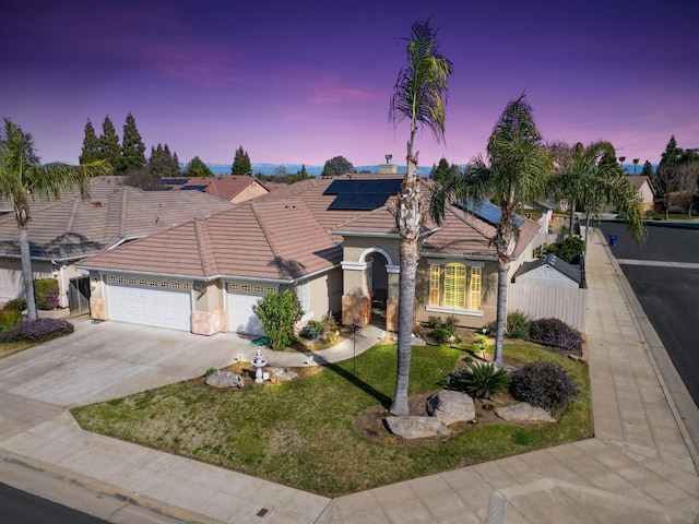 mediterranean / spanish house featuring an attached garage, fence, concrete driveway, a lawn, and roof mounted solar panels