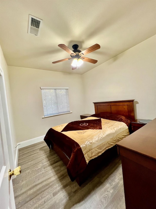 bedroom with a ceiling fan, wood finished floors, visible vents, and baseboards