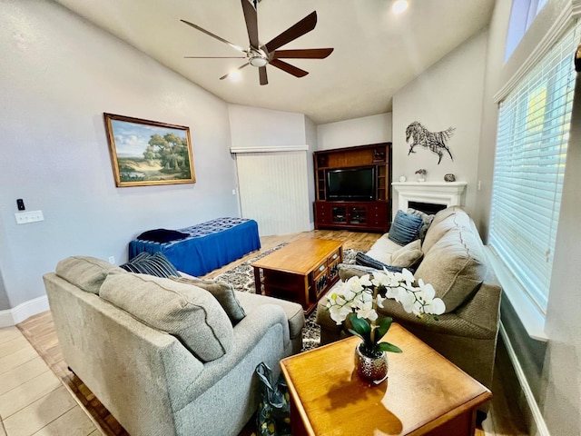 living area with a fireplace, lofted ceiling, ceiling fan, light wood-type flooring, and baseboards