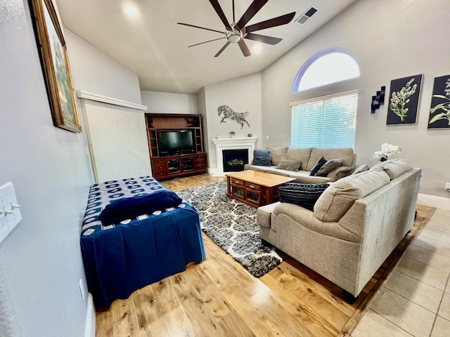 living area featuring a fireplace, light wood finished floors, visible vents, a ceiling fan, and baseboards