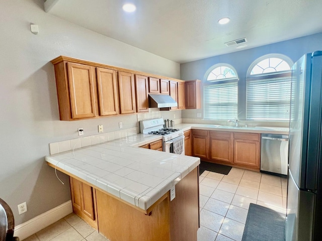 kitchen featuring tile countertops, visible vents, appliances with stainless steel finishes, a peninsula, and under cabinet range hood