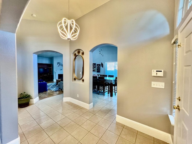 interior space featuring arched walkways, a notable chandelier, baseboards, and light tile patterned floors