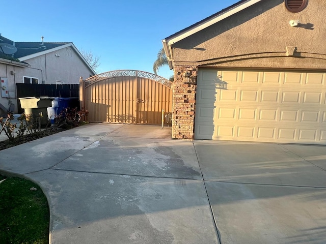 view of property exterior with a garage, driveway, brick siding, and a gate