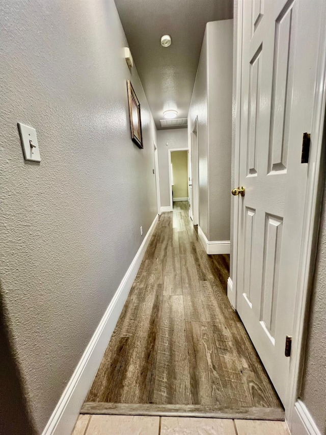 corridor with a textured wall, baseboards, and wood finished floors