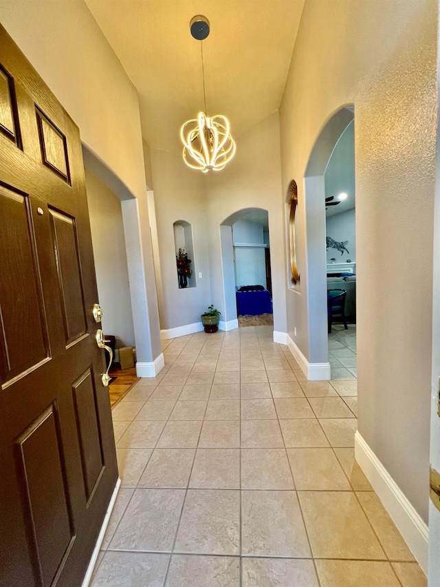 hallway with a chandelier, arched walkways, light tile patterned flooring, and baseboards