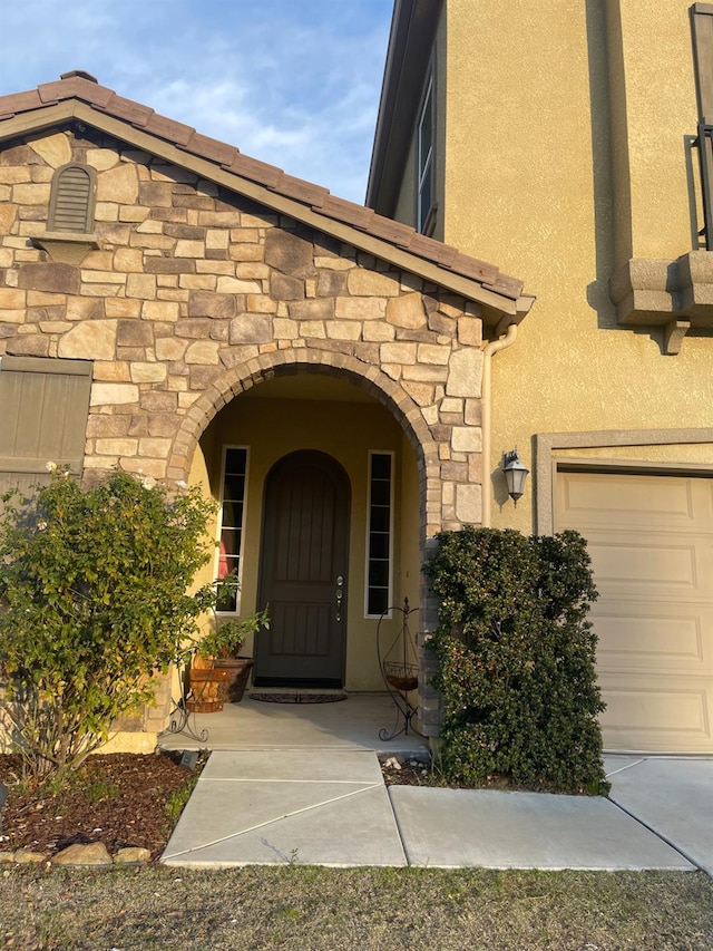 property entrance with a garage, stone siding, and stucco siding